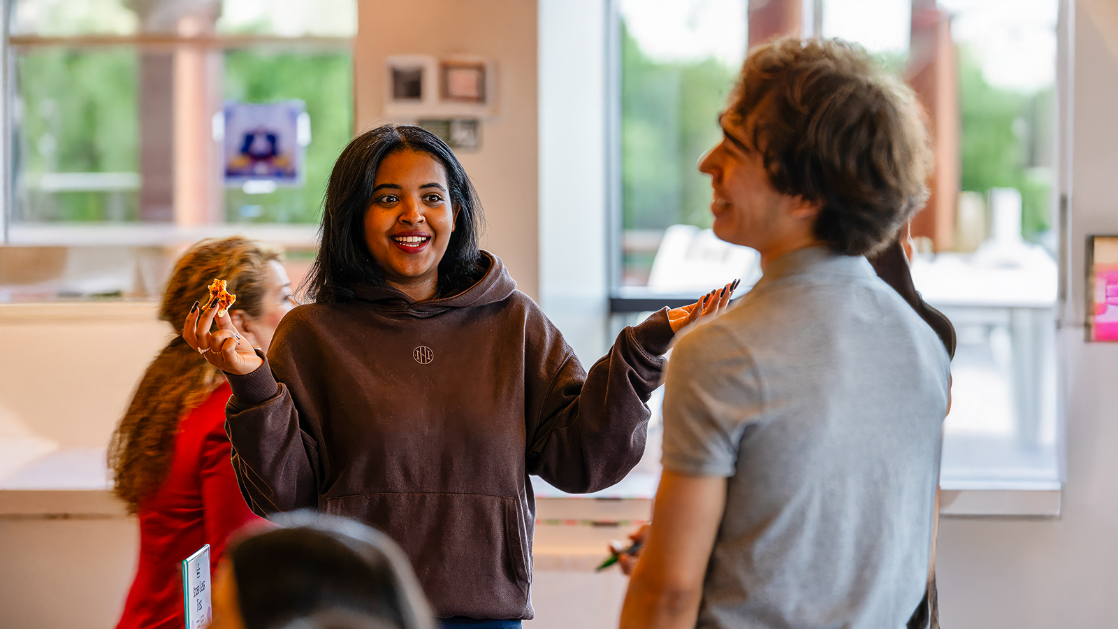 Female student with a bite in the hand smiling and talking with a male student