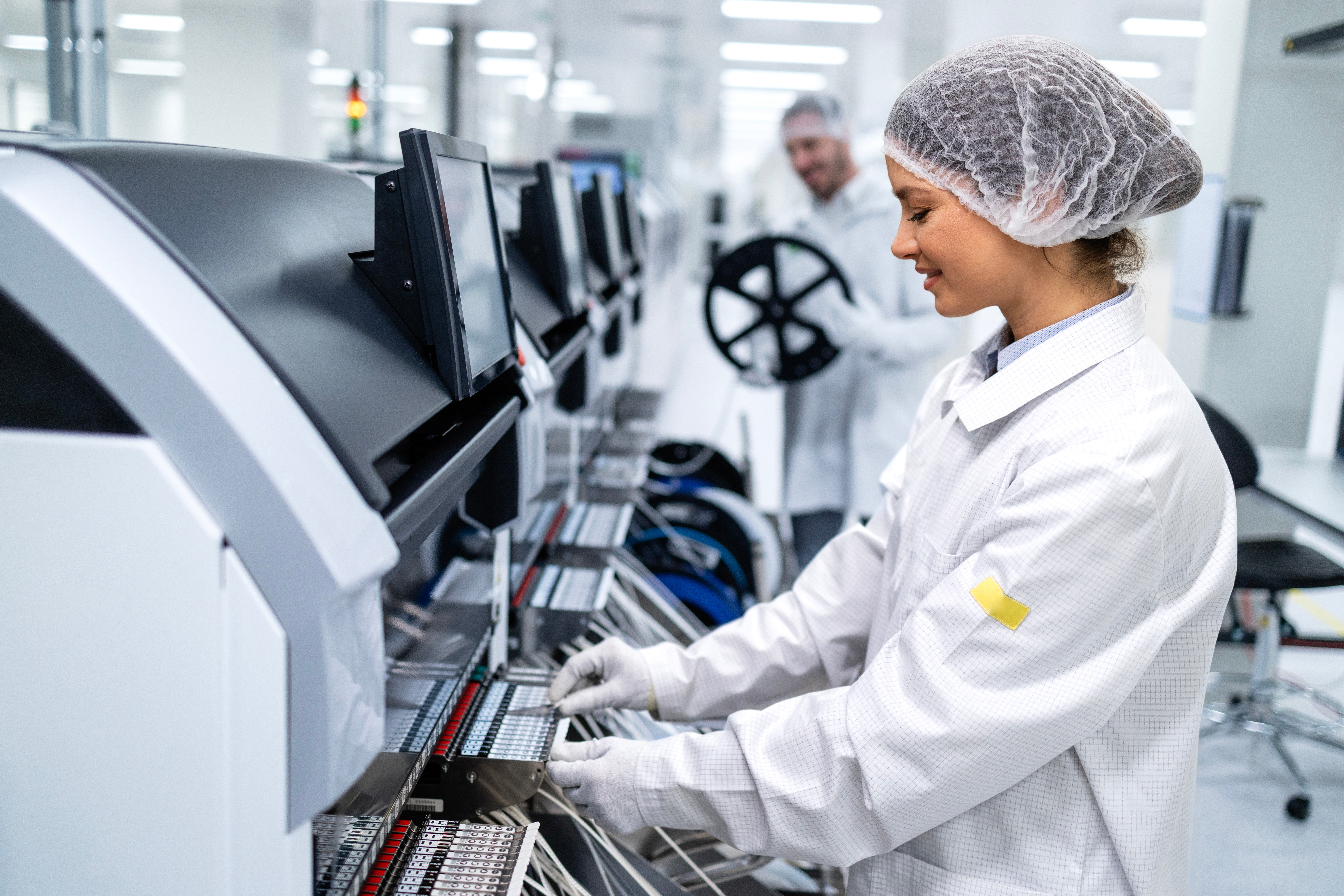Person in cleanroom clothing operates semiconductor manufacturing equipment.