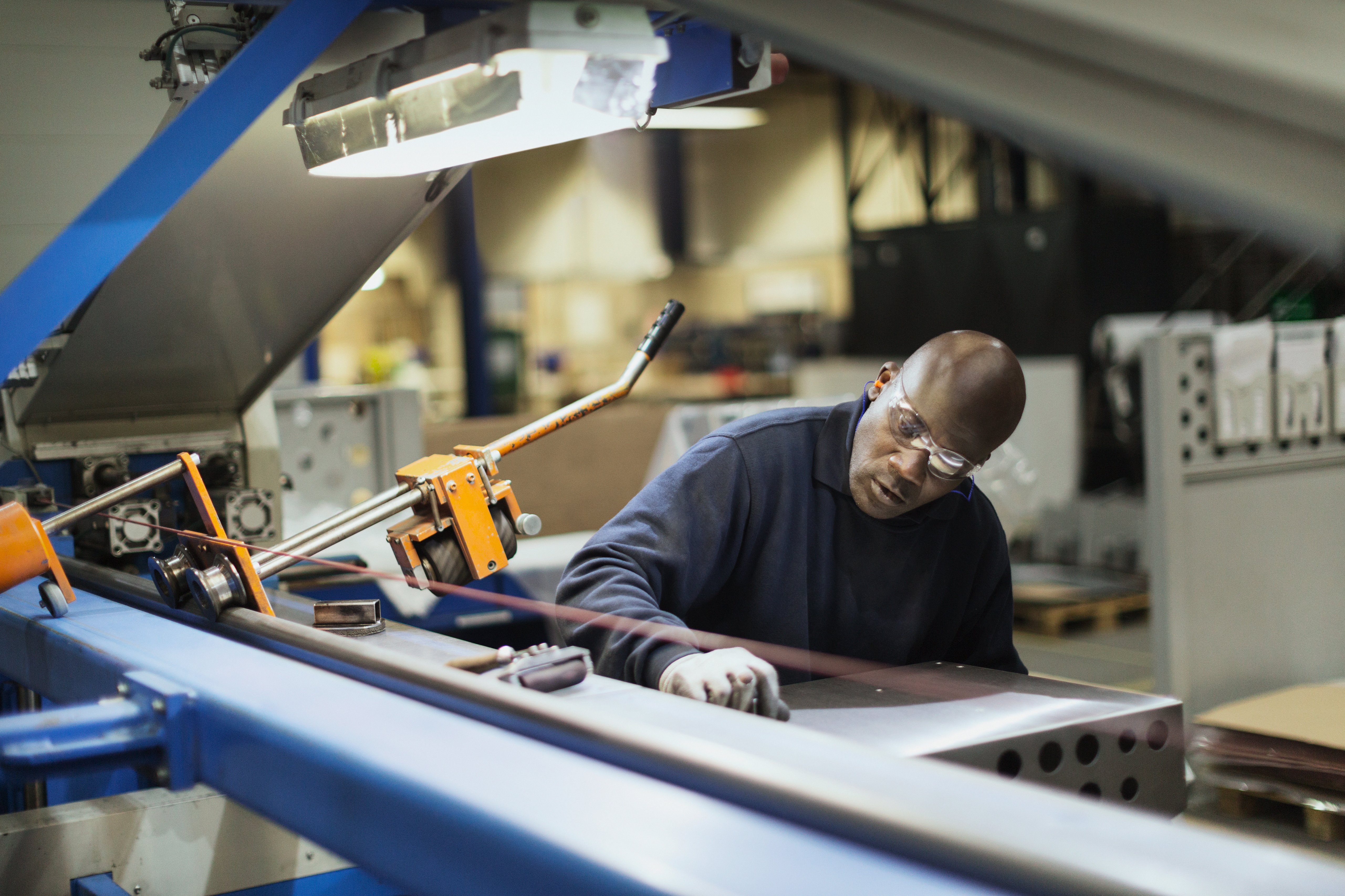 Worker in safety glasses operates sheet metal machinery in a manufacturing facility.