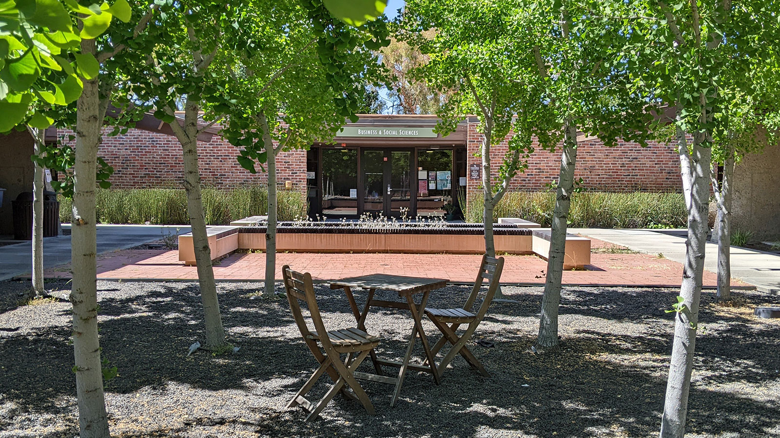 Office entrance with outdoor patio in foreground, with a table and several chairs, designed for social conversations. 