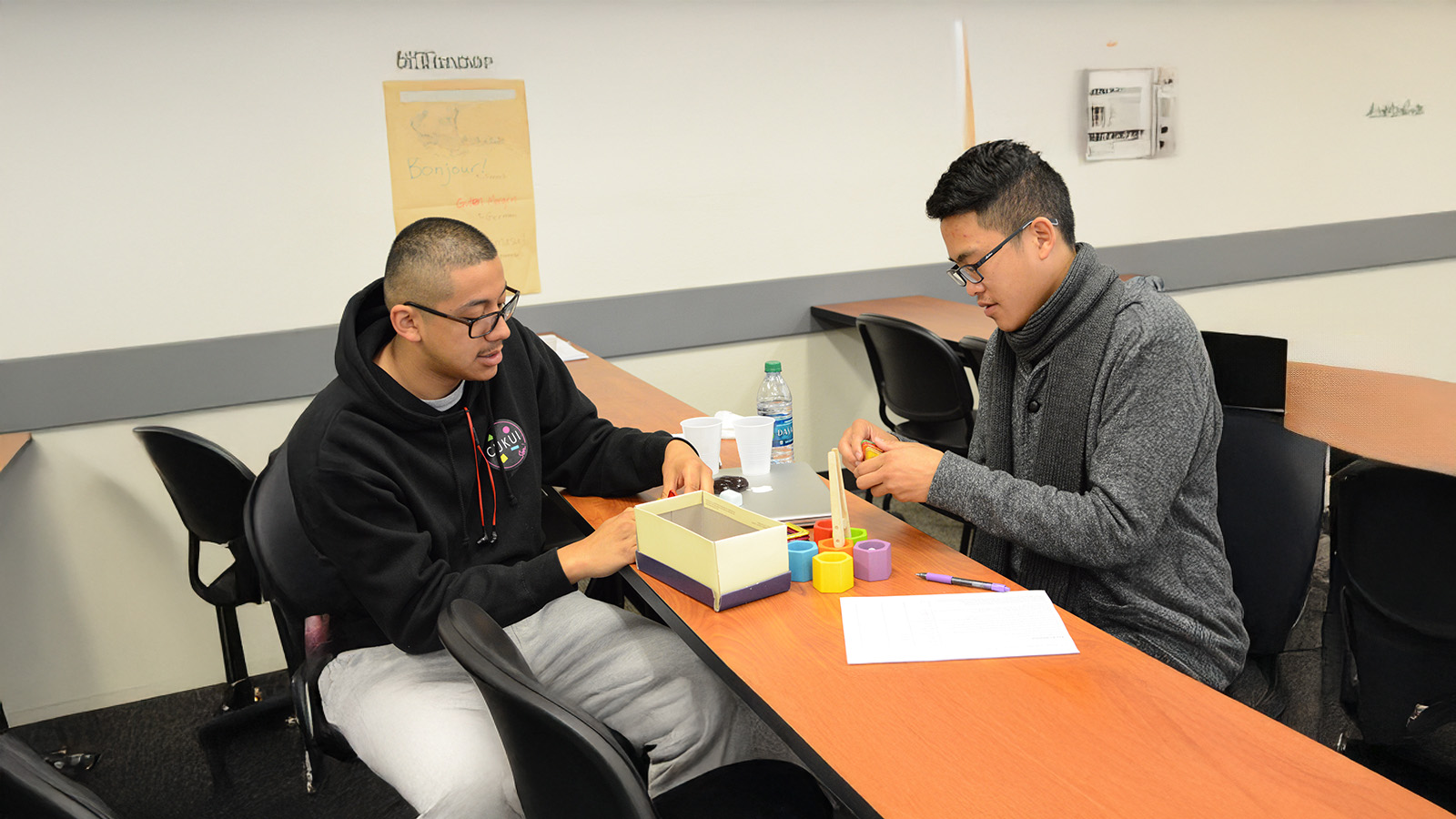 Two students sit at a classroom table working with colorful learning materials during a hands-on activity.