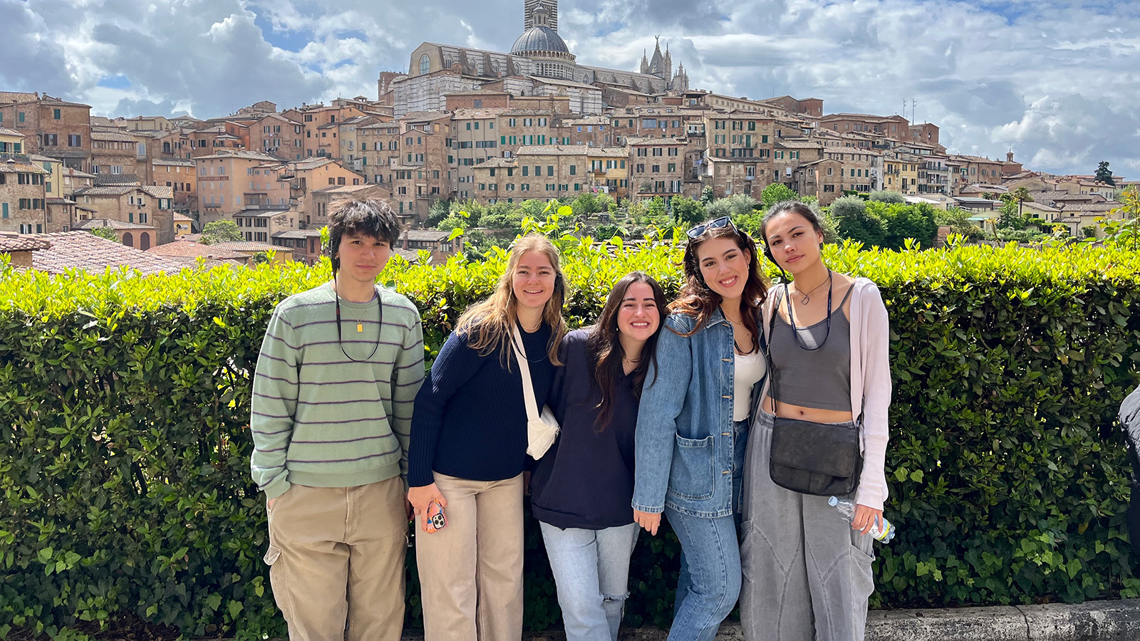 A group of students stands outdoors smiling with a historic city and cathedral in the background.