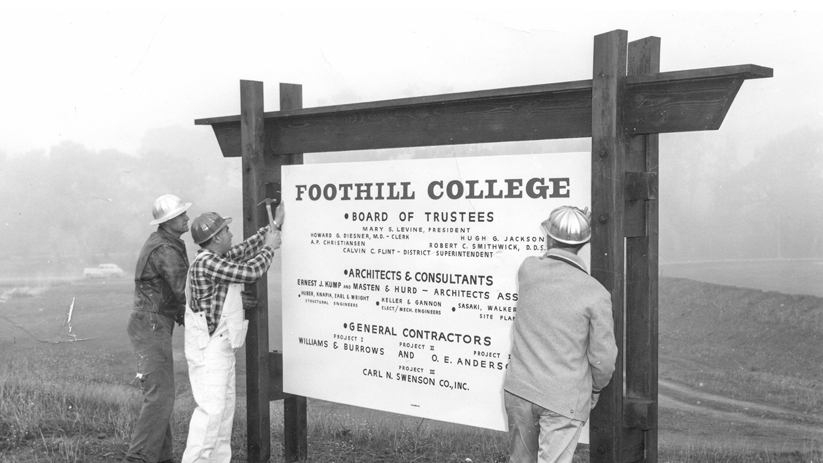 Workers in hard hats install a large Foothill College construction sign at an outdoor site.
