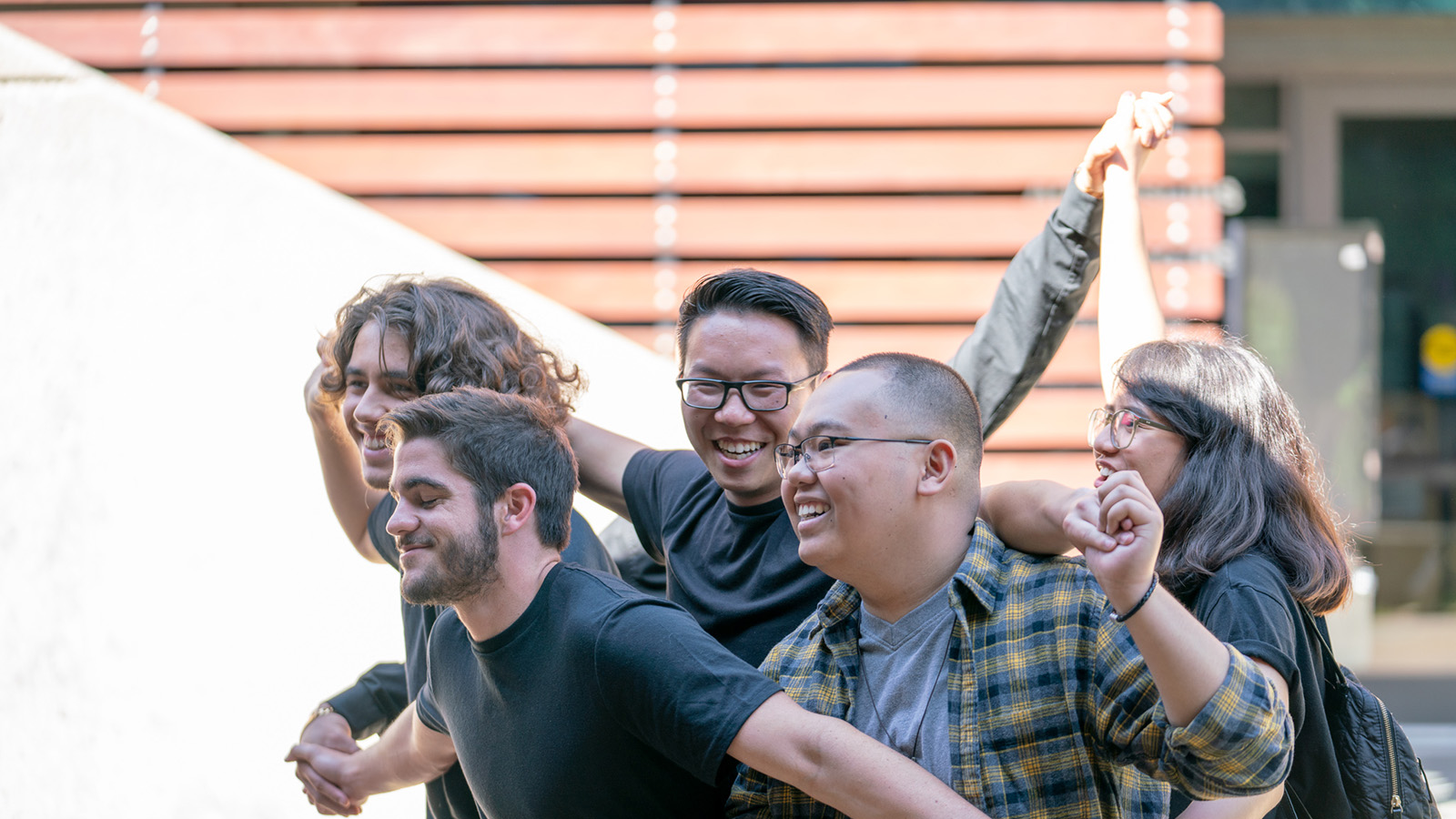 A group of students stand close together outdoors, smiling and holding each other’s arms in a cheerful, celebratory pose.