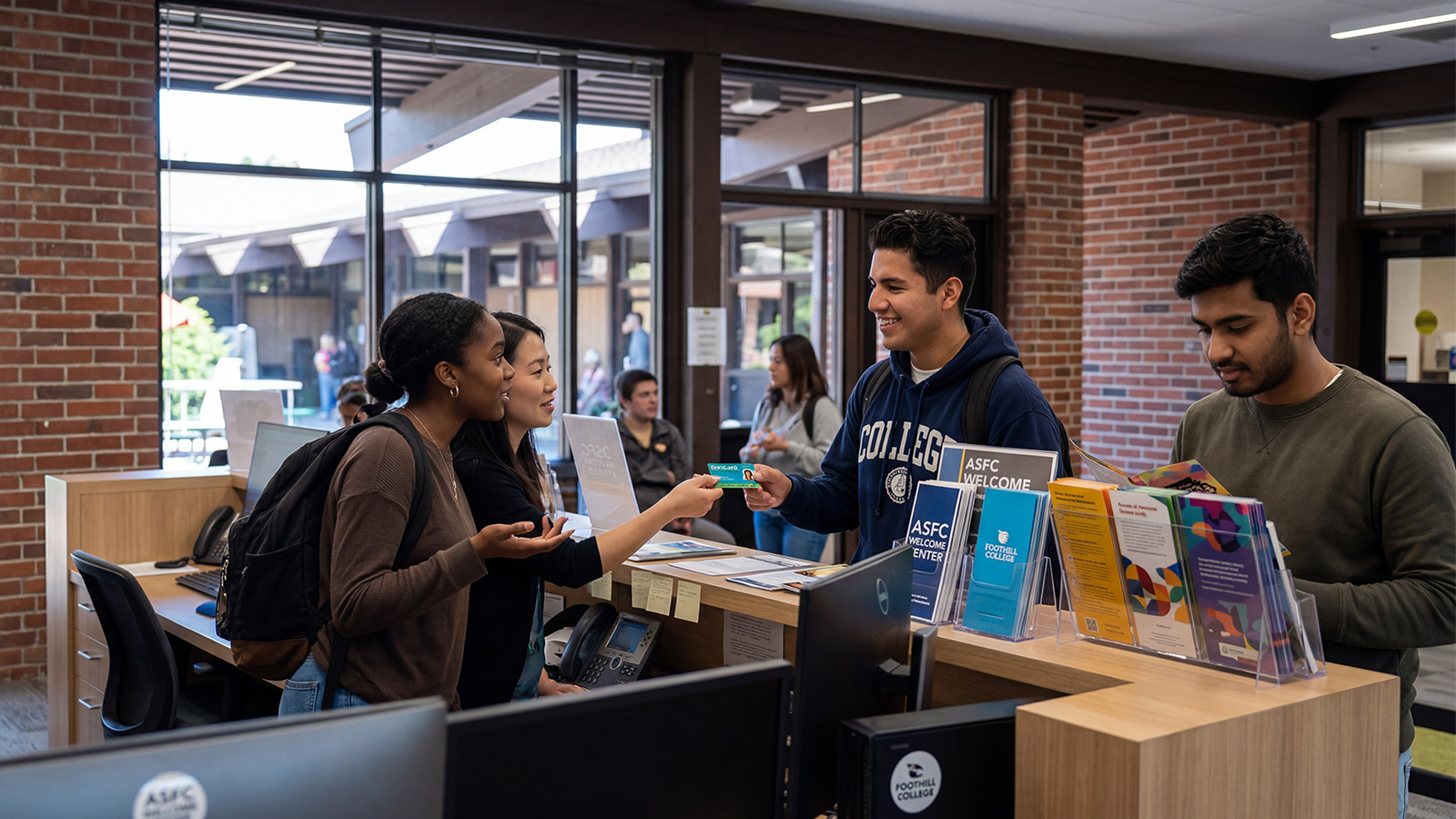 Students interacting at a campus welcome center desk, receiving assistance and information while staff provide materials and answer questions.