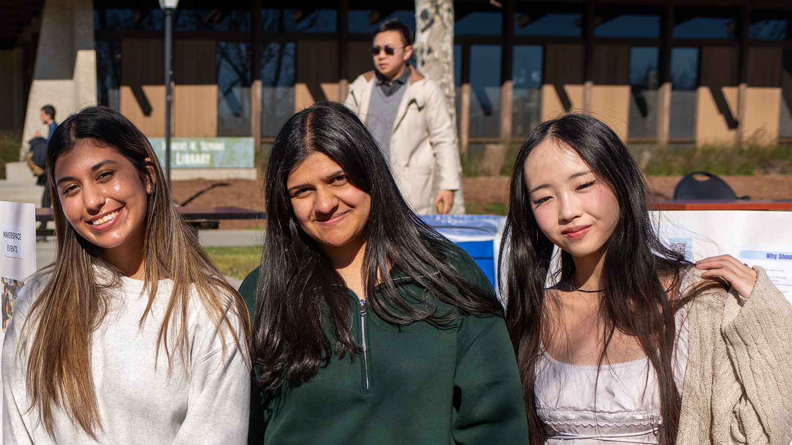 Three students stand outdoors smiling at the camera during a campus event.